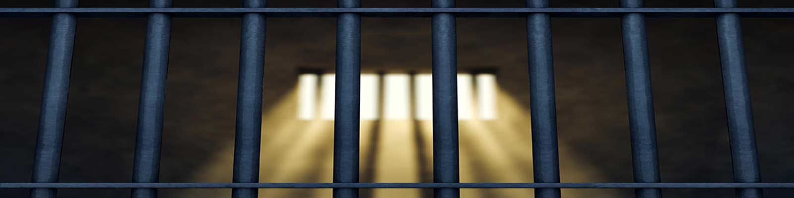 View of Barred Prison Cell Window with sun shining down from behind prison bars.