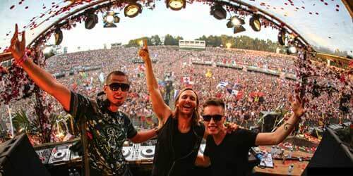 Performers on Stage taking a selfie with huge open-air audience behind them.