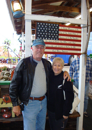 Elderly couple standing proud with the United States flag behind them.
