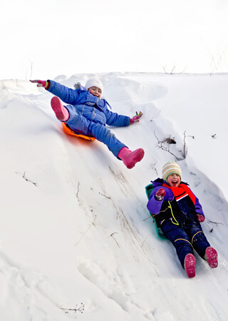 Kids sledding down a snowy hill.