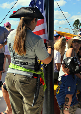 Pirate Woman hoisting up United States Flag while child looks on.